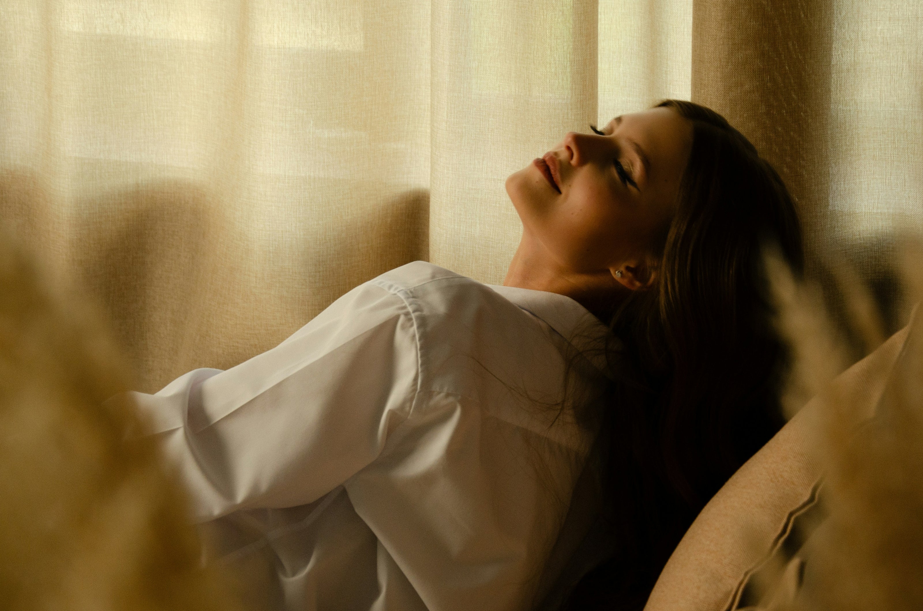 Woman leaning back and relaxing in soft natural light, representing calm and wellness for Resture sleep relaxation brand